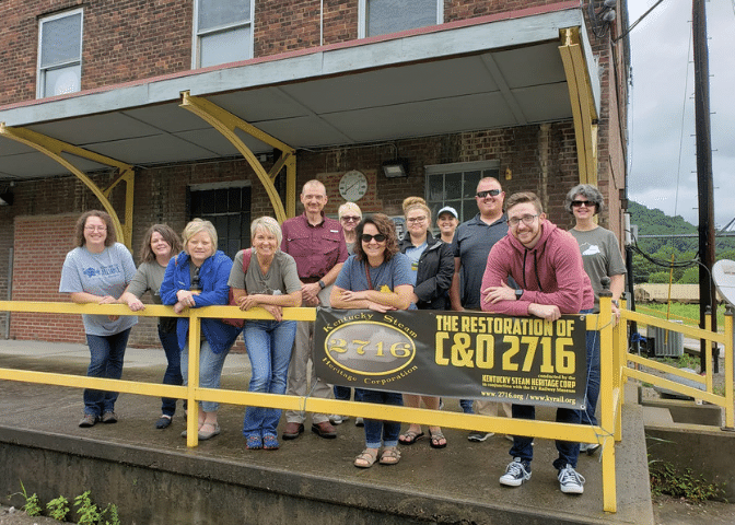 A group of leaders stand in front of a yellow rail at Kentucky Steam Heritage center in estill county kentucky.