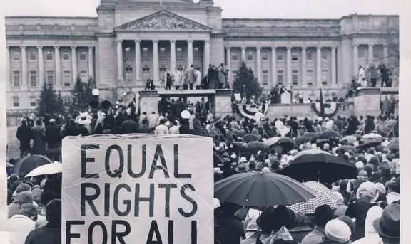 a black and white image of the 1964 march on frankfort with a crowd in front of the capitol and a sign that reads equal rights for all.