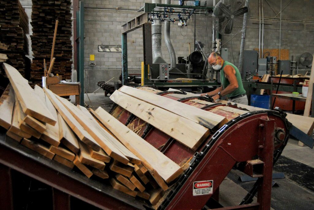 A man in a mask loads lumber onto a conveyer belt at powell valley millwork in eastern kentucky.