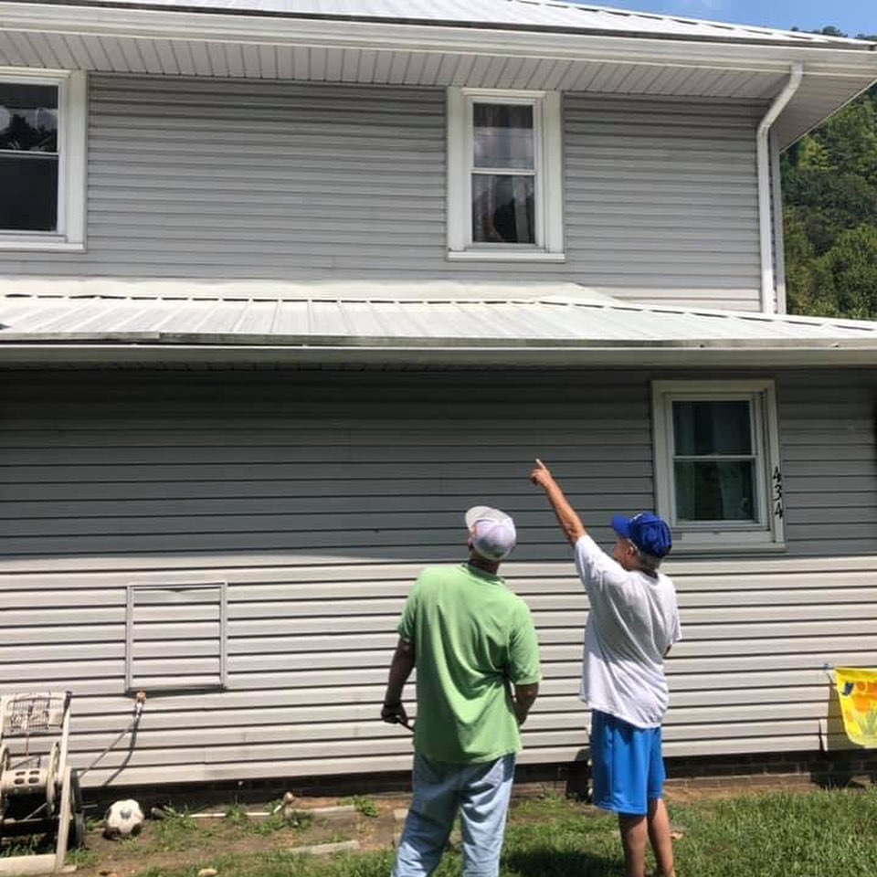 A man points up at the roof of a house in eastern kentucky, while an energy efficiency auditor stands next to him. The house is in benham ky