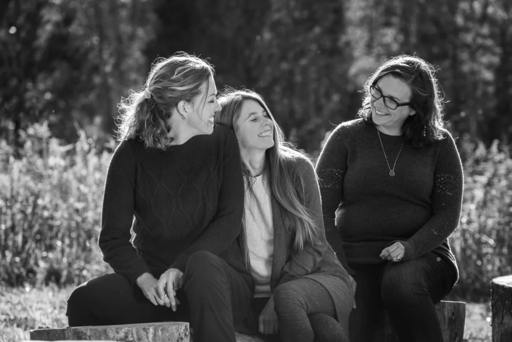 The three women who started Red Oaks sit outside on logs