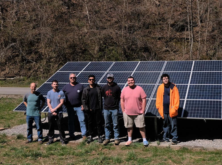 A group of students stand in front of a solar panel installation on a farm in floyd county.