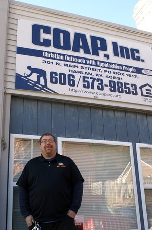 Randall Howard stands in of a sign for COAP, Inc. in Harlan, Kentucky. The housing nonprofit builds energy efficient housing and repairs homes