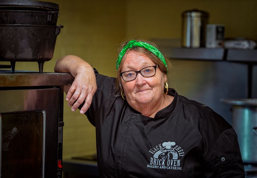 Gwen stands wearing a Black Sheep bakery shirt in the kitchen at Hemphill Community Center 