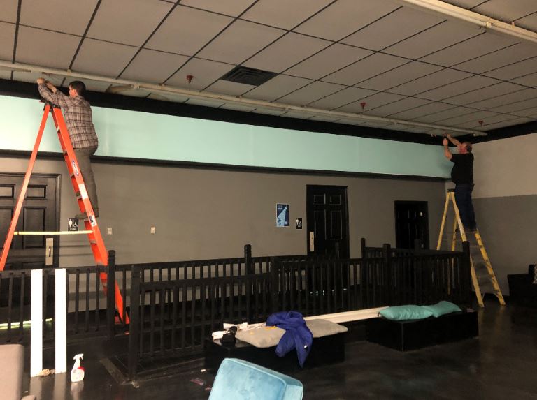 Cecil and Ben stand on ladders while working on an energy efficiency upgrade in eastern kentucky. They are MACED New Energy interns.