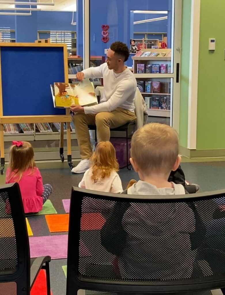 Chase Carson from Unity Allies holds a book while reading to kids at a library