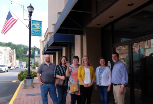 A group of people stand in front of the former first federal building with an american flag in the background. Pictured: Les Roll (Mountain Association), Bailey Richards (City of Hazard), Betsy Whaley (Mountain Association), Jaime Coffey (First Federal Savings & Loan), Robin Gabbard (LKLP, Mountain Association Board Chair), Peter Hille (Mountain Association)