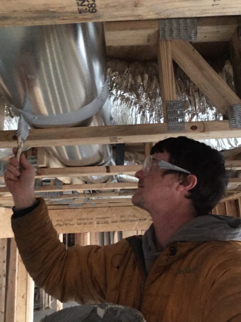 Ben Tatum uses a brush to apply sealant on a leak during an energy efficiency audit in eastern kentucky.
