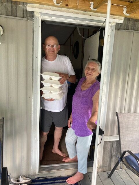 Two Eastern Kentuckians stand at their door holding boxes of food.