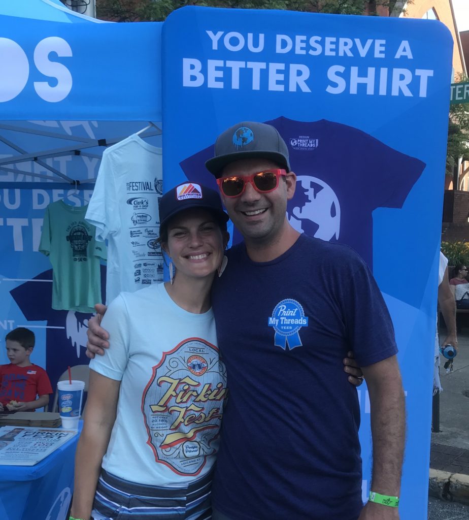 Kyle and Annie pose in front of their booth for Print My Threads. They are saving thousands through energy efficiency and solar