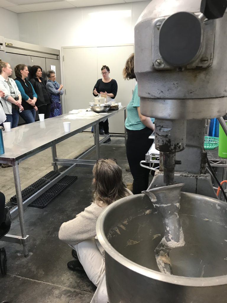 A piece of equipment in the foreground with a baking class in the background. This class was taught at the berea farm store