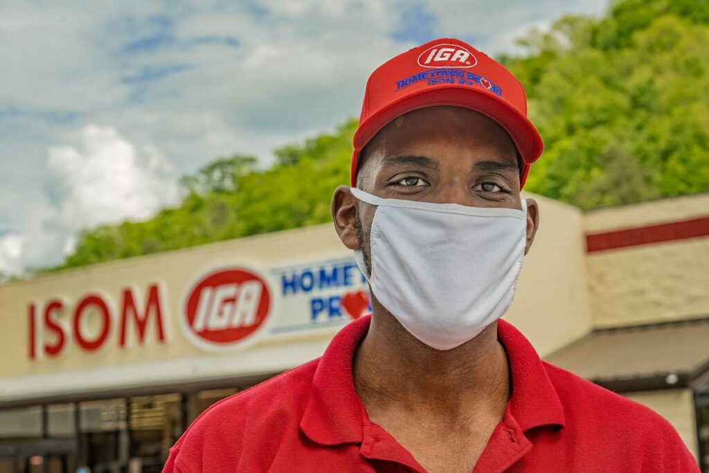 A man in a red shirt and white face mask stands in front of ISOM IGA during covid-19 in eastern kentucky.