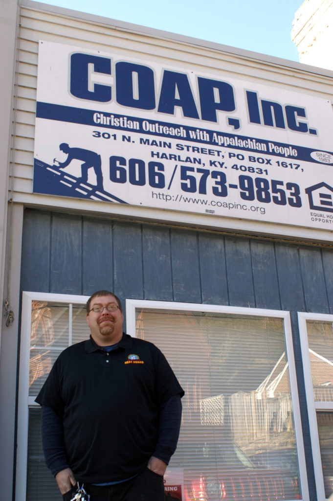 A man stands in front of a sign for COAP, inc in harlan, kentucky. MACED supports the nonprofit