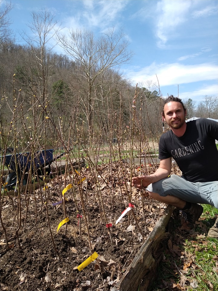 Michael sits outside next to several small trees