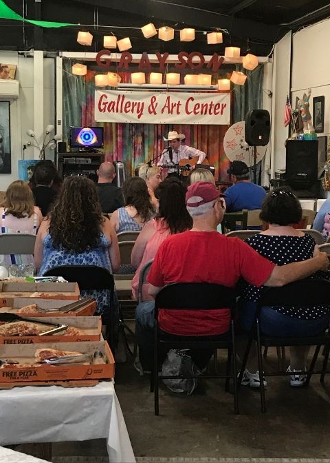 Crowd sits in chairs at Grayson Gallery and Art Center in Carter County, Kentucky. A man, Ole Justin Chambers, plays live music on stage.