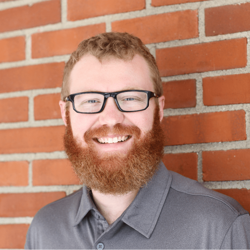 A man stands again a brick wall smiling. Zac Ebersole is preparing for his MACED new energy internship to learn about energy in kentucky