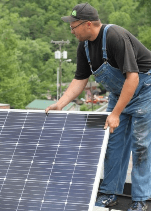 A man holds a solar panel on top of a roof in eastern kentucky. This is part of building a new energy workforce and economy in region