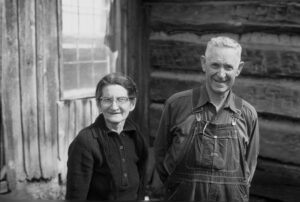Black and white  historical photo of two people standing in front of a cabin