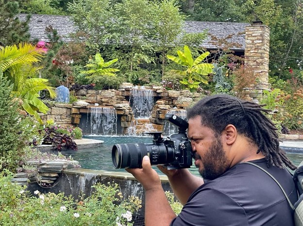 brandon turner unsung heroes takes photos at oak hill gardens, he is pictured with his camera and waterfalls in the background