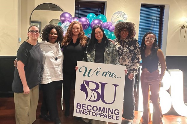 a group of women stand with a banner that says becoming unstoppable