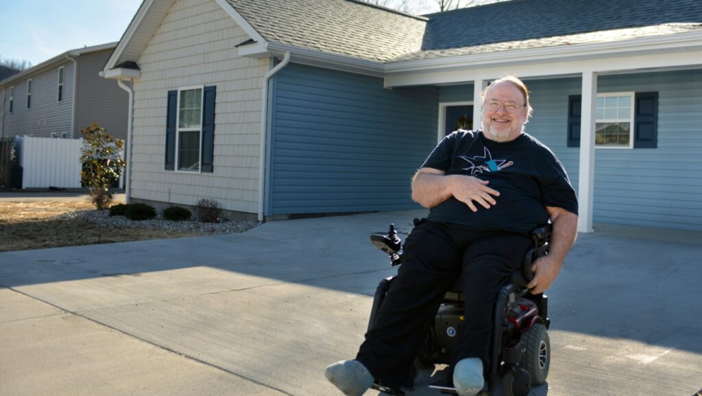 A man in a wheelchair is pictured in front of a house built by Frontier Housing in Eastern Kentucky.