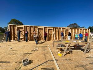 A group of people raise the wall of a house that is under construction by Frontier Housing.