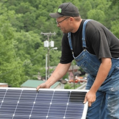 Man holds solar panel on top of a roof in the mountains of Eastern Kentucky.