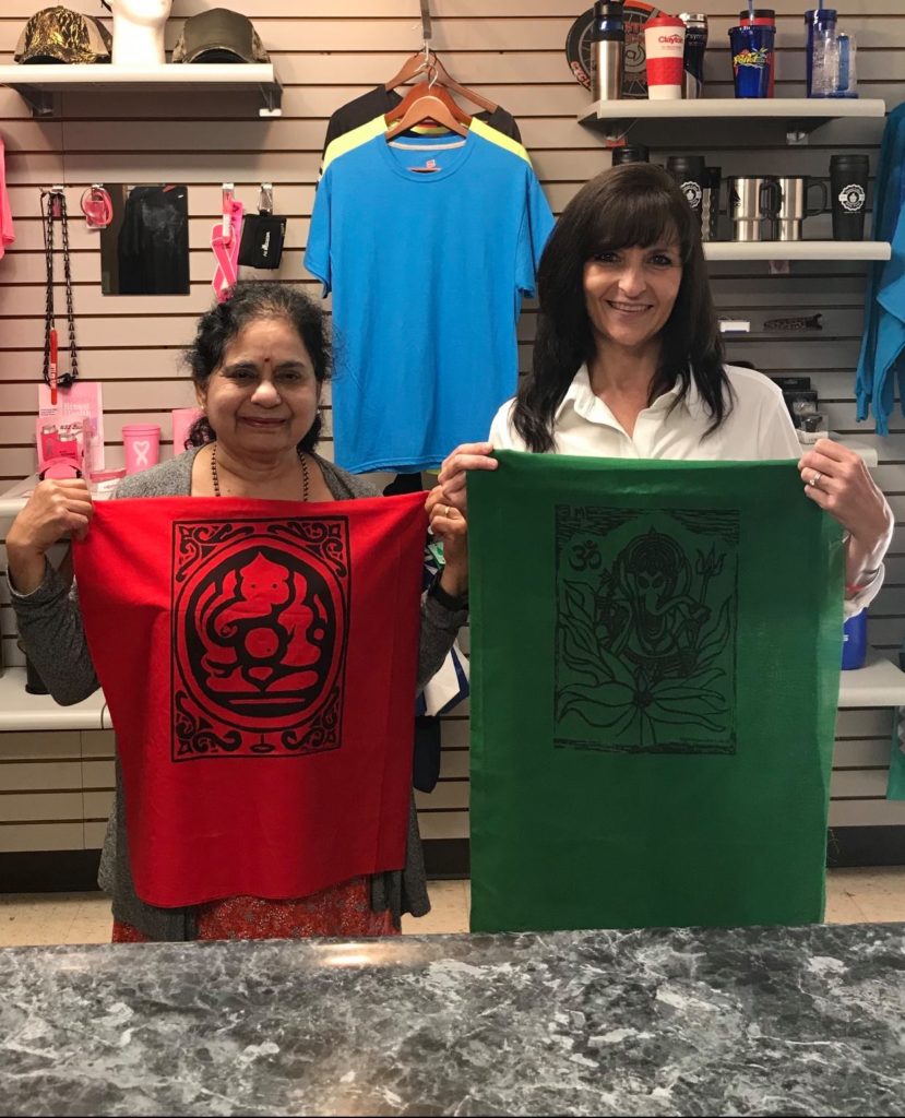 Gina Rose holds up a piece of cloth while standing with a customer at the shirt gallery in martin, kentucky.