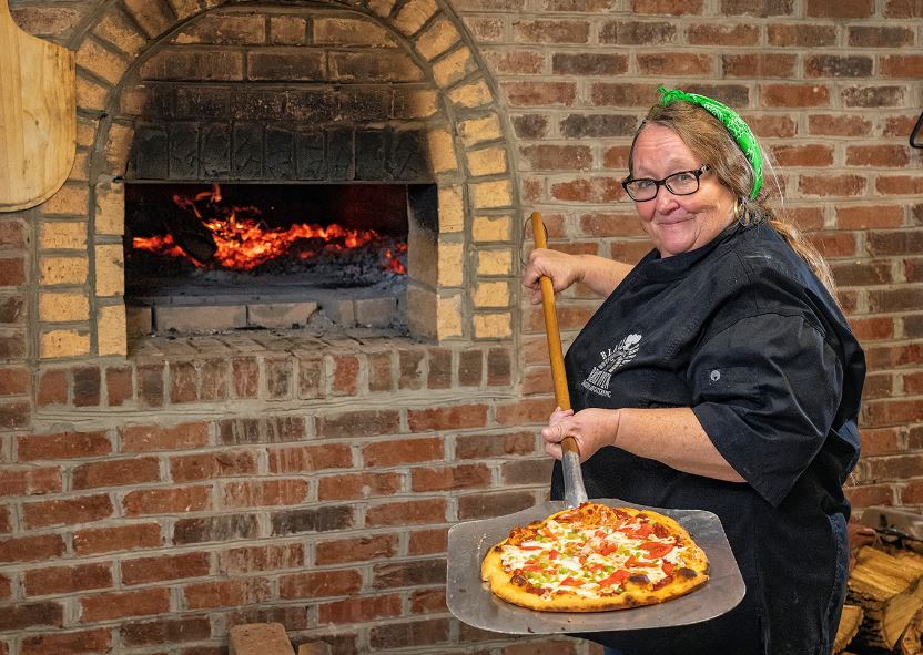 gwen johnson holds a wood fired pizza at hemphill community center for black sheep brick oven and catering. Building is powered by solar energy