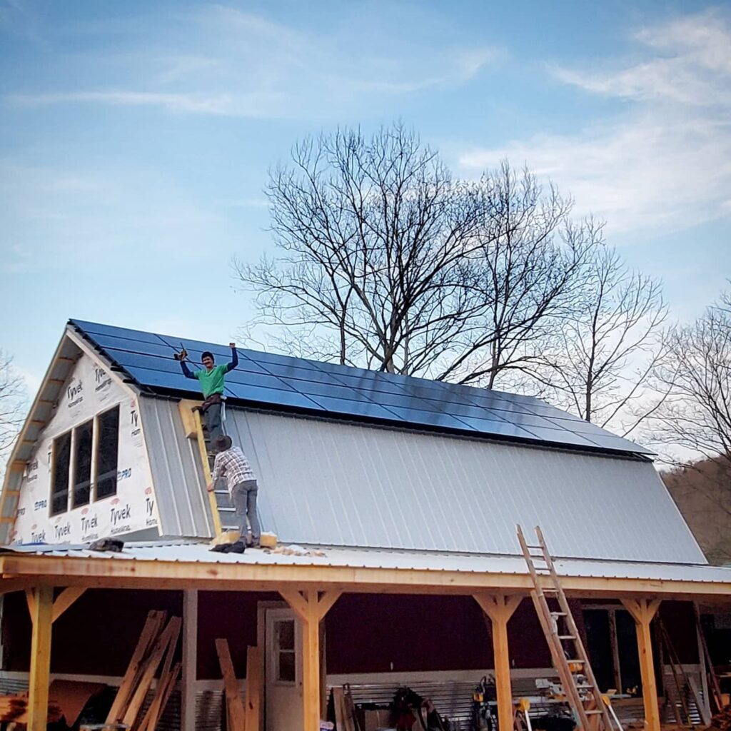 Ben Tatum stands on a ladder in front of a building with solar panels on it after finishing homegrown hideaways solar project.