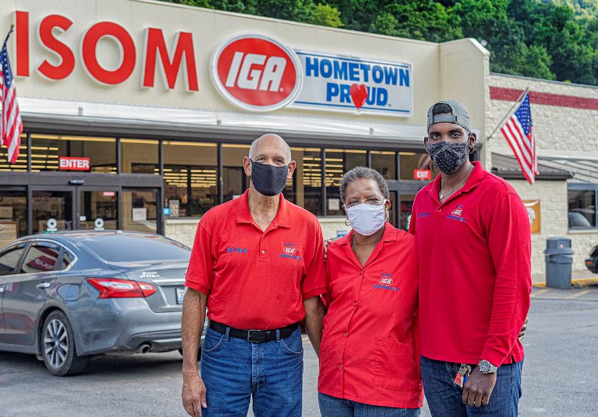 Gwen Christon stands with her son and husband in front of Isom IGA. They are wearing red shirts and face masks.