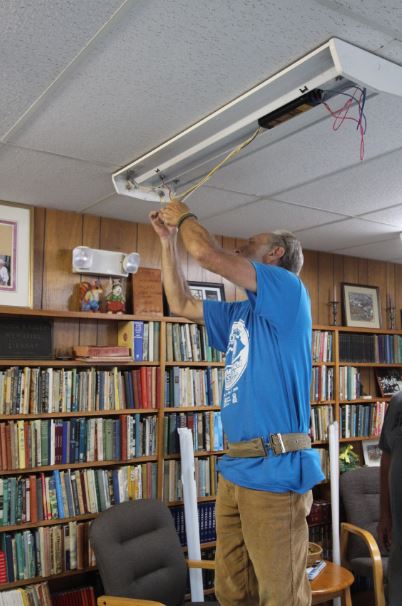 John Craft stands on a ladder while upgrading a light fixture to LED at Dessie Scott Children's Home in Wolfe County, Kentucky.