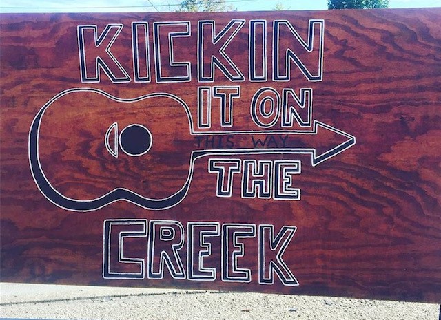 A wooden sign reads Kickin it on the creek, which is a well known festival in estill county kentucky. tyler childers typically performs here.