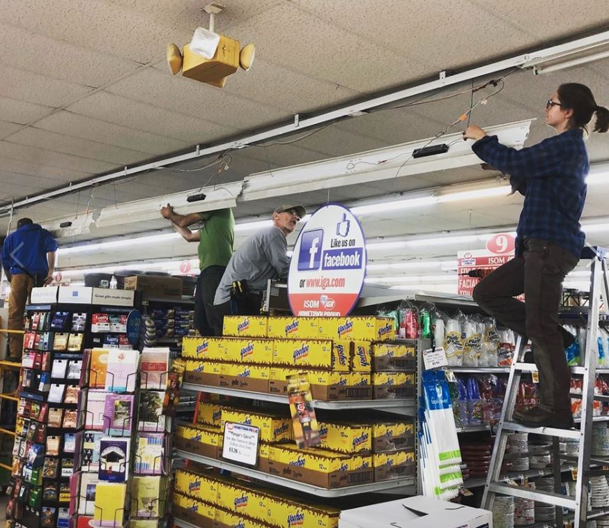 MACED employees stand on ladders to install lighting in Isom IGA as part of New Energy intern training.