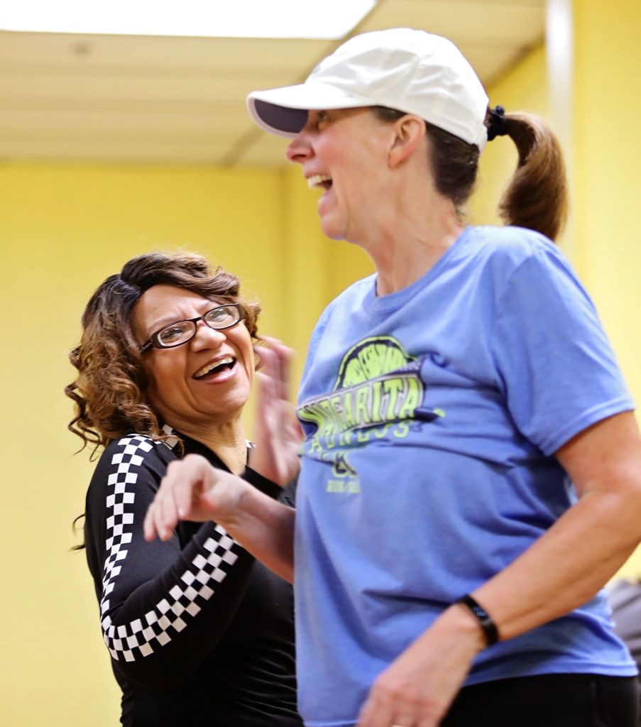 Two women high five at a fitness class in hazard, kentucky. This project is supported by the mountain association's business support.