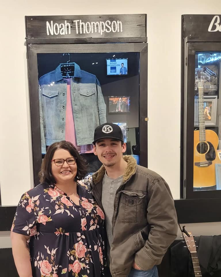 noah thompson stands with jessica blankenship infront of a display with his photos and clothes.