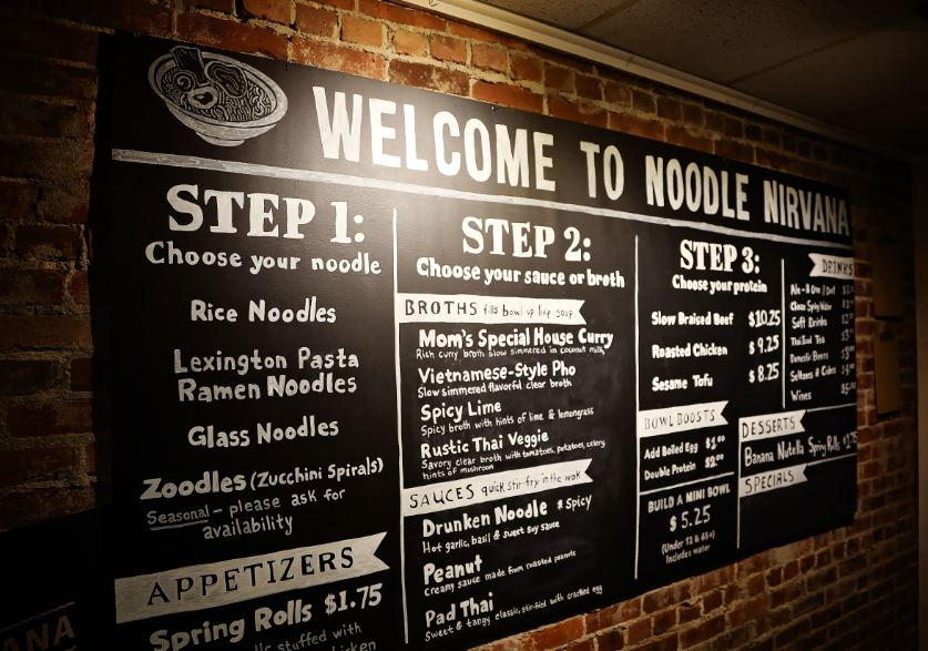 The menu board against a brick wall at Noodle Nirvana. MACED supports the business with a loan and technical assistance