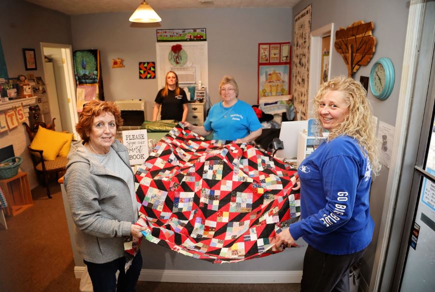 A group of women stand with a quilt and fabric inside the shop in Stanton, Kentucky, in Powell County.