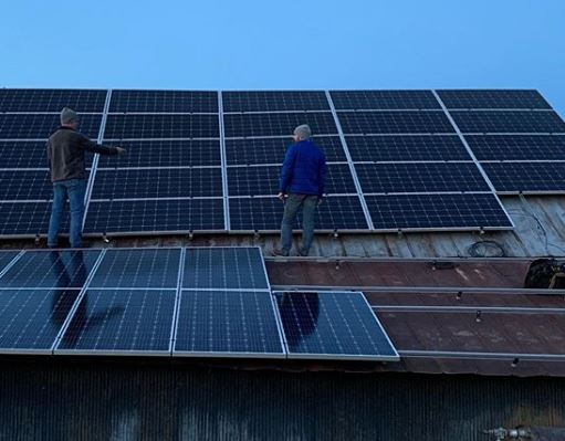 Solar being installed by two men on the Lazy Eight Stock Farm roof in Paint Lick, Kentucky.