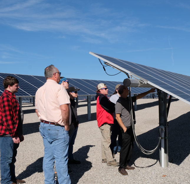 Several people listen to a man pointing at solar panels