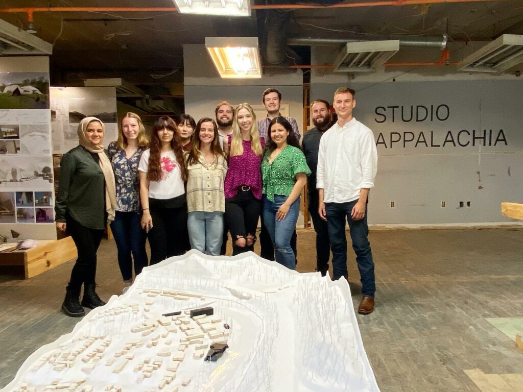 A group of students stands in front of a model of Hazard, KY. In the background the wall reads Studio Appalachia