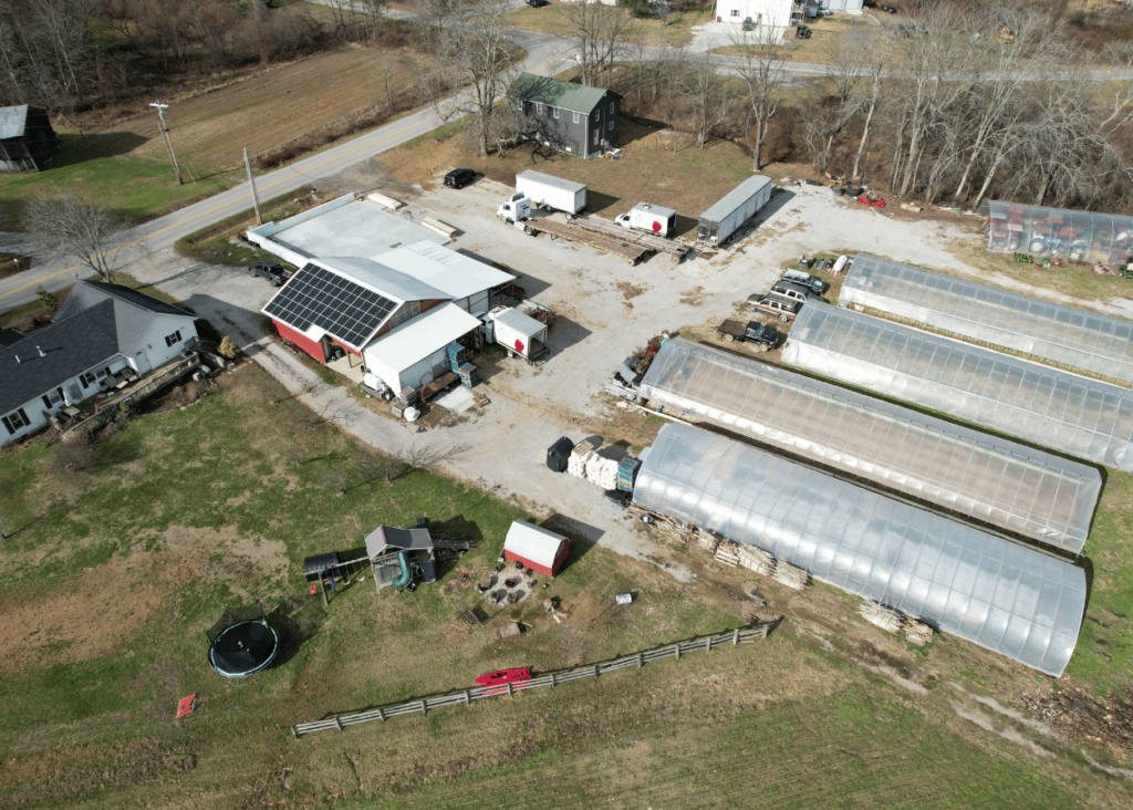 Aerial view of farm shows a barn with solar and four greenhouses and two houses