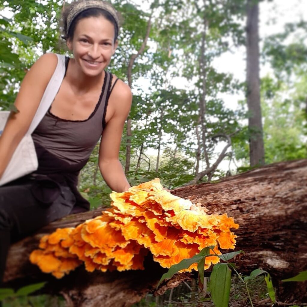 Joana is pictured in the forest with a cluster of mushrooms on a log