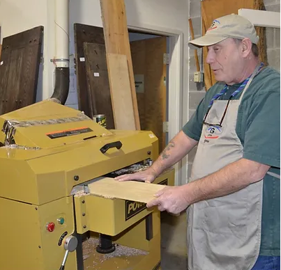 Gene king runs a piece of wood through a machine in TG Designs shop