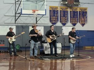 four members of a band stand and play in the community gym with their instruments