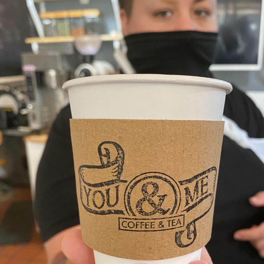 An employee wearing a mask holds a You & Me Coffee & Tea cup in corbin, kentucky.